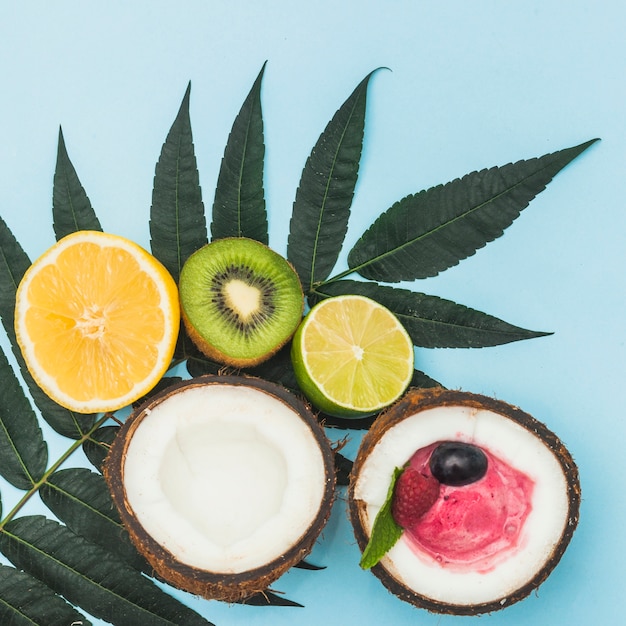 Orange coupée en deux; kiwi; citron et noix de coco avec de la crème glacée sur des feuilles vertes sur fond bleu Photo gratuit