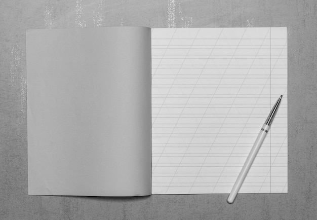 Ouvrez le cahier d'écolier dans une ligne étroite avec une barre oblique pour apprendre l'orthographe, créez une copie avec espace copie et un stylo à bille sur fond gris, vue de dessus, photo en noir et blanc Photo Premium