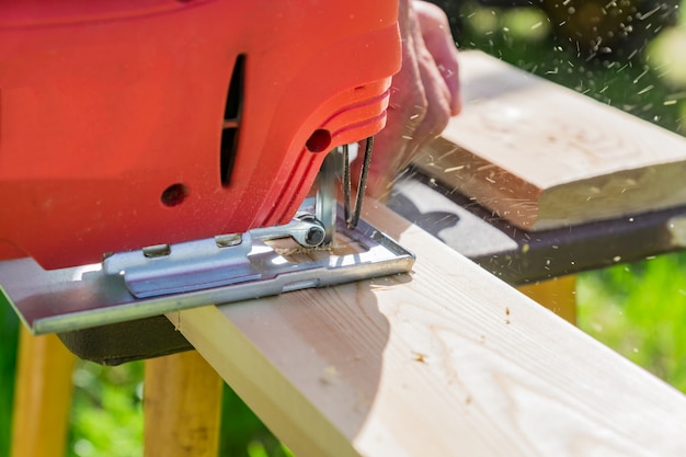 Ouvrier en bois couper un panneau en bois avec une scie sauteuse à l'extérieur, vue rapprochée d'un homme travaillant avec une scie sauteuse électrique et une planche en bois Photo Premium