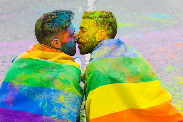 Une paire de homosexuels peints s'embrassant enveloppés dans un drapeau arc-en-ciel lors du défilé de la fierté lgbt Photo gratuit