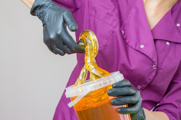 Pâte de sucre ou miel de cire à épiler avec des gants noirs, mains du cosmétologue au salon spa Photo Premium