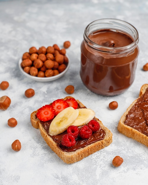 Pâte à tartiner au chocolat ou crème de nougat aux noisettes dans un bocal en verre sur du béton, fond Photo gratuit
