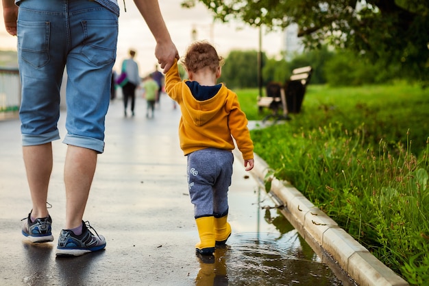 Père et fils marchant dans l'air frais en bottes de caoutchouc sur les flaques d'eau après la pluie le jour d'été. Photo Premium
