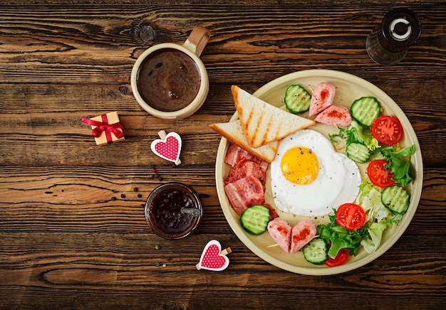 Petit Déjeuner Le Jour De La Saint-valentin - œuf Au Plat En Forme De Coeur, Toasts, Saucisse, Bacond De Légumes Frais. Petit Déjeuner Anglais. Tasse De Café. Vue De Dessus Photo gratuit