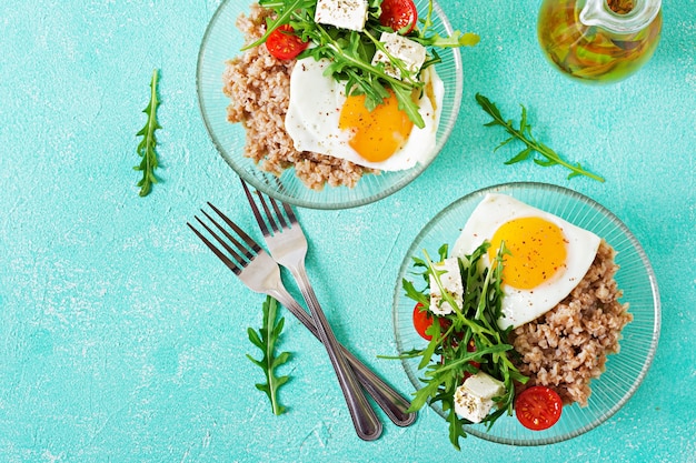 Petit-déjeuner Sain Avec Oeuf, Fromage Feta, Roquette, Tomates Et Bouillie De Sarrasin Sur Fond Clair. Nutrition Adéquat. Menu Diététique. Mise à Plat. Vue De Dessus Photo gratuit
