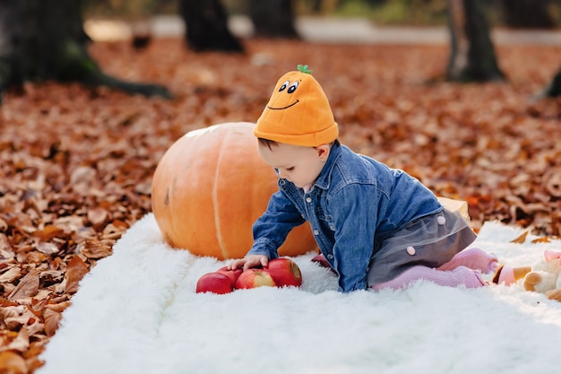 Petit enfant mignon dans le parc sur une feuille jaune avec citrouille en automne Photo Premium
