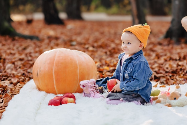 Petit enfant mignon dans le parc sur une feuille jaune avec citrouille en automne Photo Premium