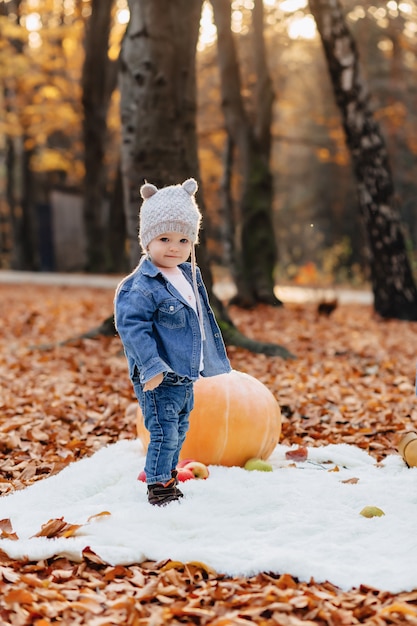 Petit enfant mignon dans le parc sur une feuille jaune avec citrouille en automne Photo Premium