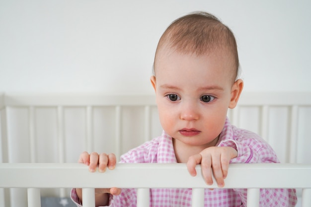 Un Petit Enfant En Pyjama Rose Est Debout Dans Le Berceau L Enfant S Est Reveille Et Attend Que Ses Parents Le Sortent Du Berceau Bebe Commence A Pleurer Photo Premium