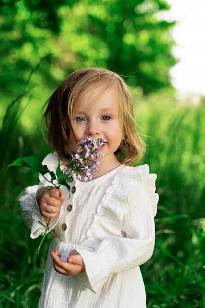 Petite Fille Aux Yeux Verts Dans Un Jardin Vert Avec Une Fleur Lilas Se Penche Sur Le Cadre Photo Premium