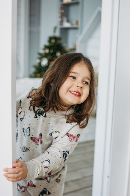 Petite Fille Brune Heureuse En Pyjama Confortable Regarde De La Chambre Des Enfants Le Temps De Noel Photo Premium