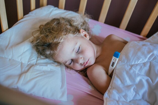 Petite Fille Dormant Sur Un Oreiller Dans Son Lit Avec Le Thermometre Photo Premium