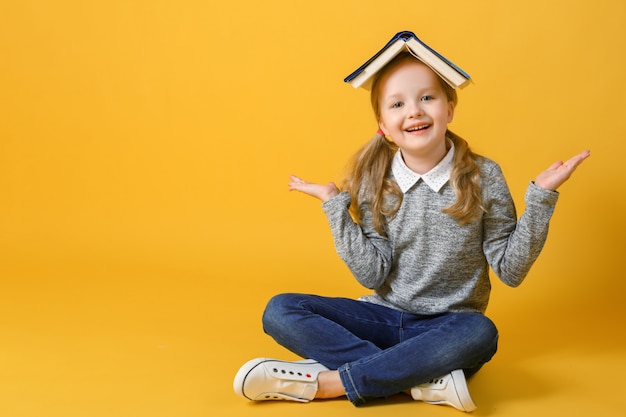 Petite fille étudiante est assise avec un livre sur la tête. Photo Premium