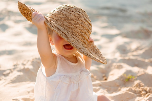 Petite Fille En Vetements Blancs Et Un Chapeau De Paille Est Assis Sur Le Sable Blanc Sur La Plage En Ete Photo Premium