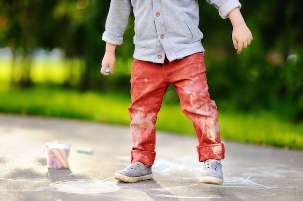 Photo gros plan du petit garçon enfant dessiner à la craie de couleur sur l'asphalte. Photo Premium