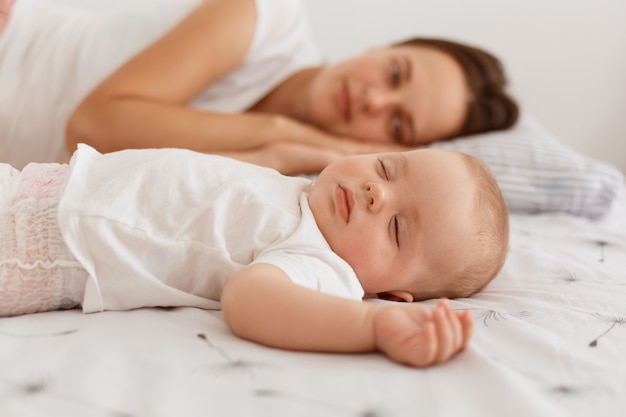 Photo D Interieur D Une Jolie Femme Aux Cheveux Noirs Portant Un T Shirt Blanc Allonge Sur Le Lit Avec Son Bebe Se Reposant Ensemble Maman Regardant Sa Jolie Fille Photo Gratuite