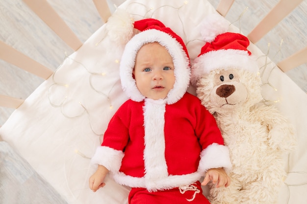 Photo De Noel D Un Bebe Dans Un Costume De Pere Noel Couche Dans Un Berceau A La Maison Avec Un Jouet Dans Un Chapeau De Pere Noel Photo Premium