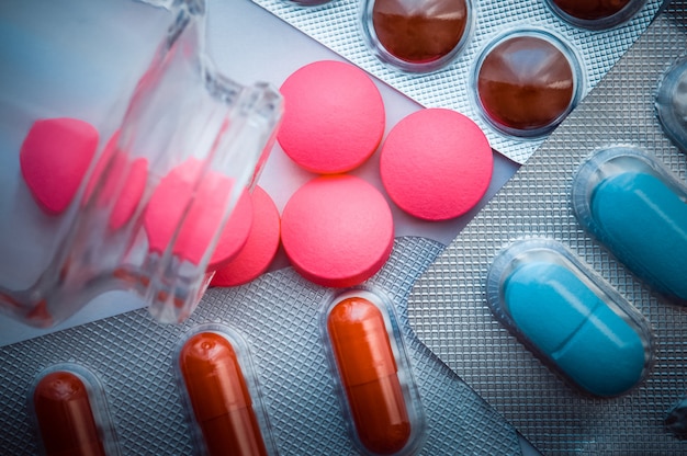 Les pilules roses sont versées à partir d'un bocal en verre et des ampoules de comprimés colorés sont dispersées sur un fond blanc Photo Premium