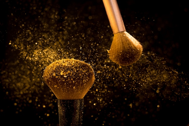 Pinceau de maquillage avec poudre cosmétique dorée se répandant sur fond noir Photo Premium