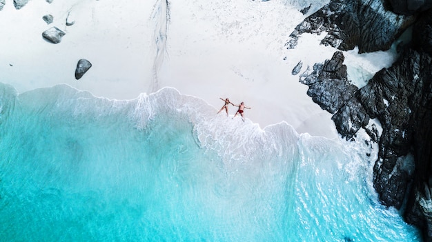 Plage de drone vue île tropicale, plage blanche avec vagues, couple allongé sur la plage Photo Premium
