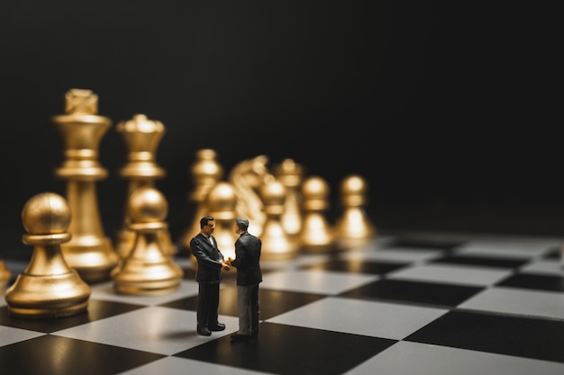 Poignée de main miniature homme d'affaires sur l'échiquier avec fond d'échecs or. Photo Premium