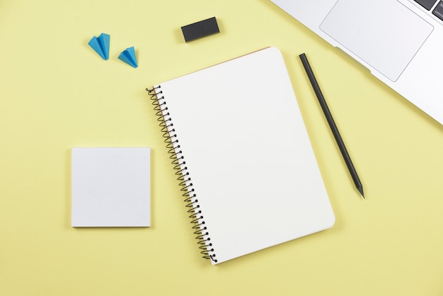 Portable; crayon; cahier à spirale; bloc-notes adhésif; avion et gomme sur fond jaune Photo gratuit
