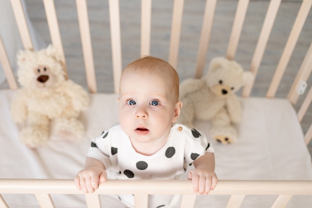 Portrait D Un Bebe De 8 Mois Debout Dans Un Berceau Avec Des Jouets En Pyjama