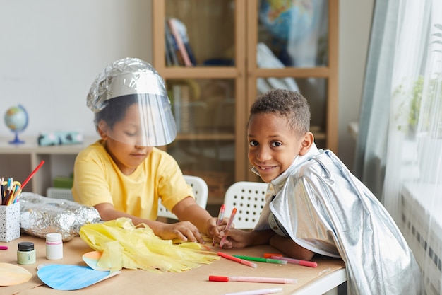 Portrait de deux garçons afro-américains faisant des combinaisons spatiales tout en profitant d'une leçon d'art et d'artisanat à l'école maternelle ou dans un centre de développement Photo Premium