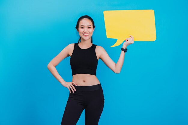 Portrait de femme confiante de remise en forme asiatique belle debout après l'exercice et tenant discours de bulle jaune vide. Photo Premium