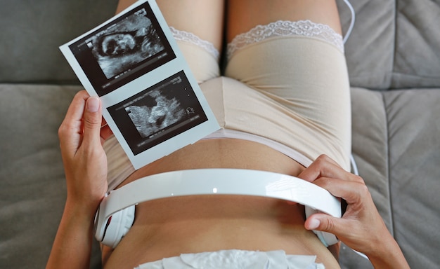 Portrait de femme enceinte assise sur un canapé à la maison tenant un film à ultrasons Photo Premium