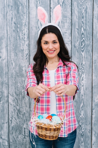 Portrait de femme souriante montrant le panier d'oeufs de pâques sur fond en bois Photo gratuit