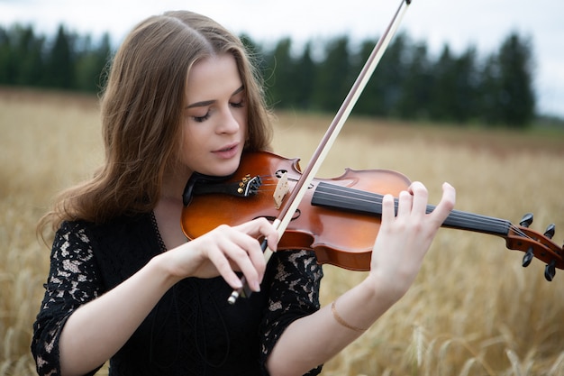 Portrait En Gros Plan D Une Jeune Femme Avec Un Leger Sourire Et Les Yeux Baisses Qui Joue Du Violon Dans Un Champ De Ble Photo Premium