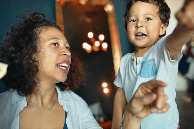 Portrait Horizontal De La Belle Jeune Femme Metisse Aux Cheveux Boucles S Amusant A L Interieur Avec Son Adorable Petit Garcon Excite Photo Gratuite