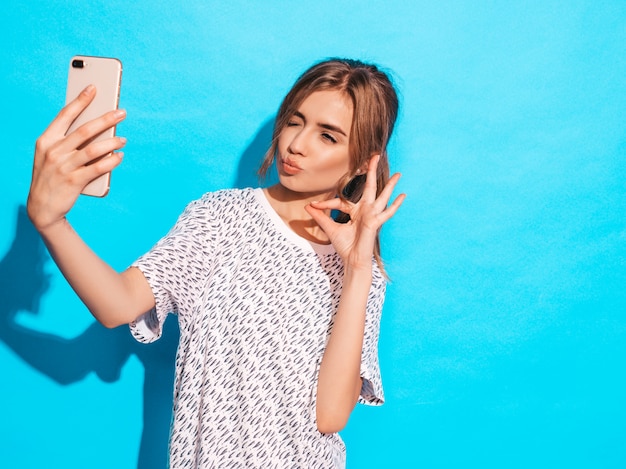 Portrait De Jeune Femme Joyeuse Prenant Selfie Photo. Belle Fille Tenant La Caméra Du Smartphone. Modèle Souriant Posant Près Du Mur Bleu En Studio. Affiche Le Signe Ok. Clins D'œil Et Fait Face Au Canard Photo gratuit