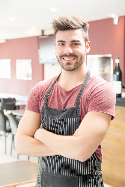 Portrait de jeune homme souriant avec tablier debout dans le bar Photo gratuit