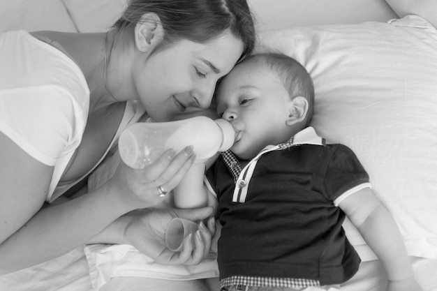 Portrait Noir Et Blanc D Une Belle Jeune Femme Nourrissant Son Bebe A Partir D Une Bouteille De Lait Sur Le Lit Photo Premium