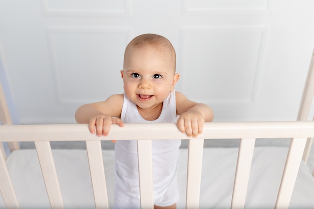 Portrait Of A Smiling Baby Boy 8 Mois Debout Dans Un Berceau Dans Une Chambre D Enfants En Vetements Blancs Et L Bebe Du Matin Concept De Produits Pour Bebe Photo Premium