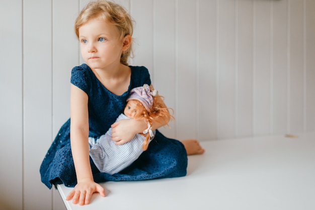 Portrait De Petite Fille Mignonne Tient Sa Belle Barbie Se Trouve Dans La Chambre De Bebe Lumineuse Regarde De Cote Photo Premium