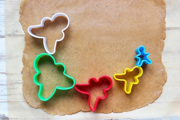 Processus de traitement des biscuits de pain d'épice, utilisez le moule de pain d'épice de coupe de pain d'épice sur du papier sulfurisé autour de découpeurs de biscuits colorés sur une table en bois blanche. vue de dessus Photo gratuit