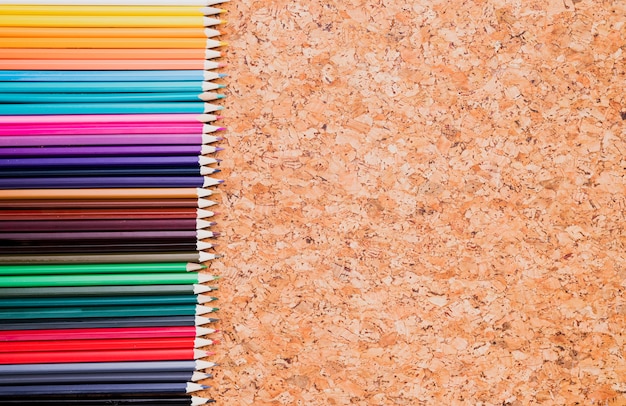 Rangée de crayons de couleur sur la vue de dessus du fond de liège Photo gratuit