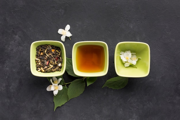 Rangée d'ingrédients de thé en bonne santé et de fleurs de jasmin blanc sur une surface noire Photo gratuit