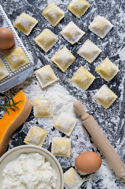 Raviolis crus traditionnels à la citrouille sur une table en bois avec de la farine, faits à la main, procédé de cuisson Photo Premium