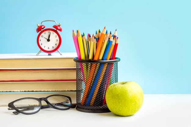 Réveil rouge, pomme, crayons de couleur, livres sur bleu Photo Premium