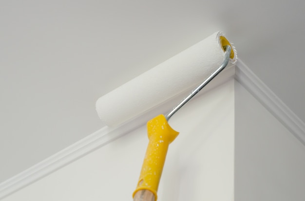 Rouleau à peinture avec manche jaune. procédé de peinture au plafond et au mur. blanc . fond Photo Premium