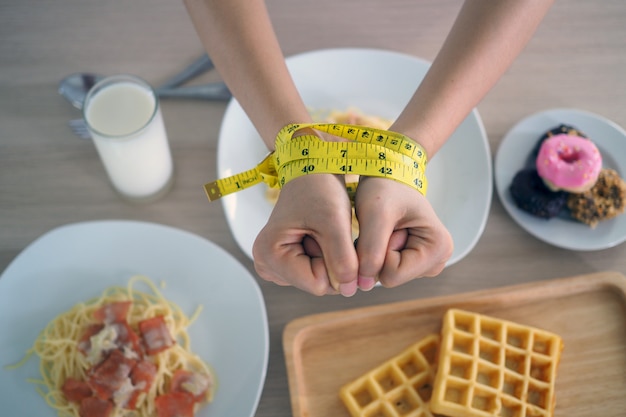 Ruban à mesurer autour des bras des femmes. arrêtez de manger des gras trans, des spaghettis, des beignets, des gaufres et des sucreries. perdre du poids pour une bonne santé. concept de régime vue de dessus Photo Premium