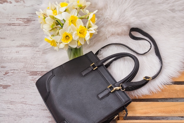Sac femelle noir sur fourrure blanche, un bouquet de jonquilles. concept à la mode Photo Premium