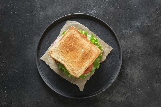 Sandwich au bacon, tomate, oignon, salade sur fond noir. isolé. vue d'en-haut. Photo Premium