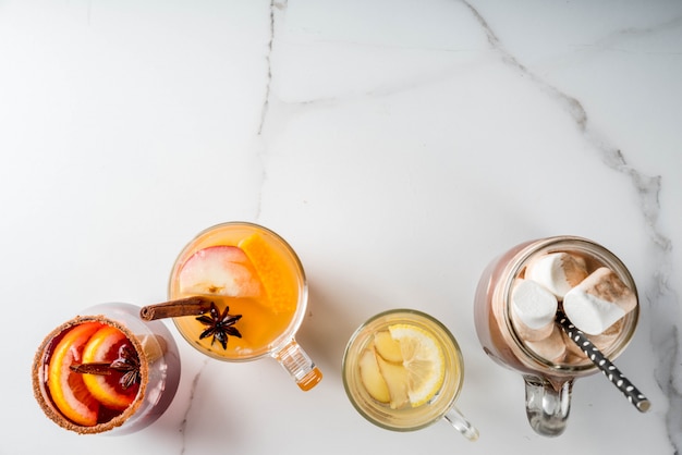 Sélection De Diverses Boissons Traditionnelles D'automne: Chocolat Chaud à La Guimauve, Thé Au Citron Et Au Gingembre, Sangria épicée à La Citrouille Blanche, Vin Chaud. Sur Une Table En Marbre Blanc, Vue Du Dessus Photo Premium
