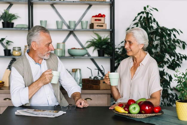 Senior couple assis dans la cuisine prenant son petit déjeuner ensemble Photo gratuit