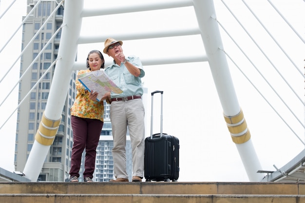 Senior couple est debout tenant la carte pour rechercher des destinations dans les rues. Photo Premium